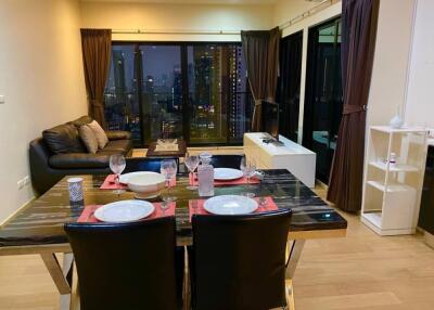 Modern living area with dining table and sofa set near large windows overlooking cityscape