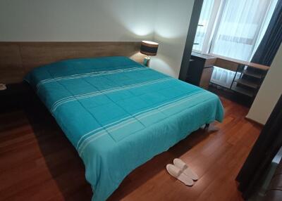 Spacious bedroom with wooden flooring, a large bed with a blue duvet, and a nightstand lamp next to the bed.