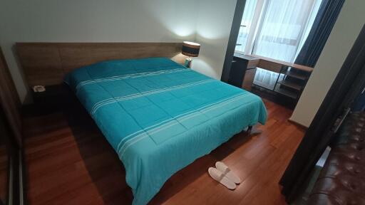 Spacious bedroom with wooden flooring, a large bed with a blue duvet, and a nightstand lamp next to the bed.