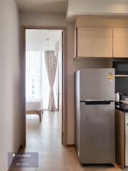 View of a kitchen area with a refrigerator and adjoining doorway leading to a bedroom