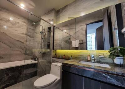 Modern bathroom with marble walls and countertop, glass shower, bathtub, toilet, and sink