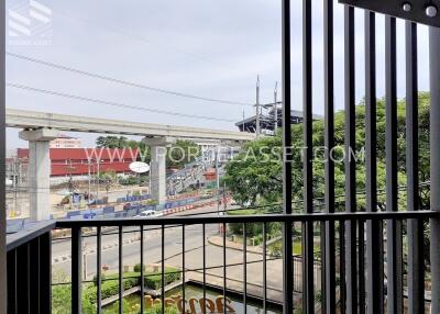 View from a balcony with railings overlooking a road, construction site, and greenery