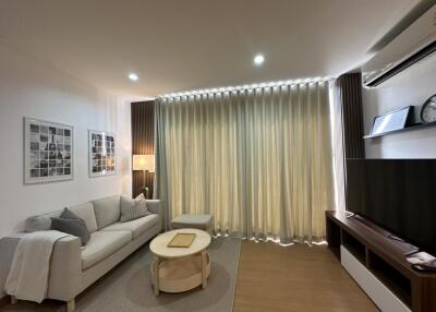 A modern living room with a sofa, coffee table, wall-mounted TV, and floor-to-ceiling curtains