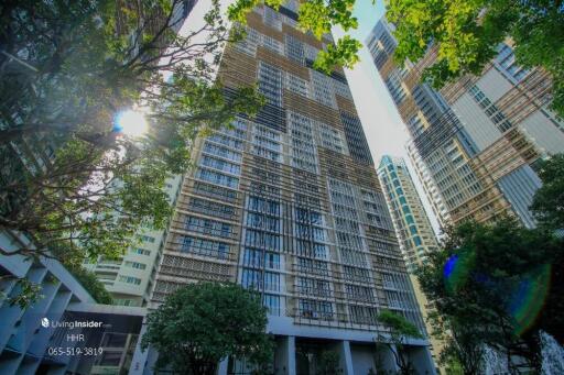 Exterior view of a modern apartment building with tall structure and surrounding greenery