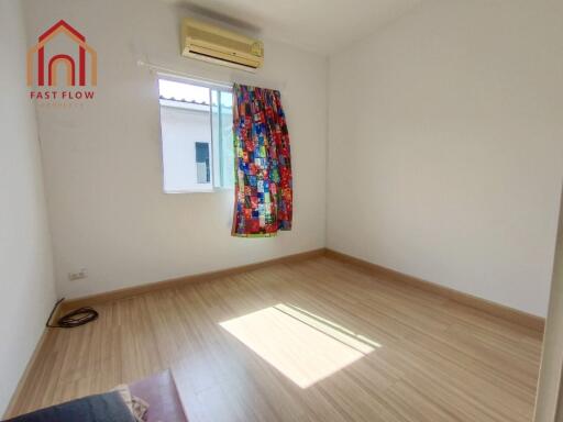 Bedroom with wooden floors, window with colorful curtain, and air conditioning unit