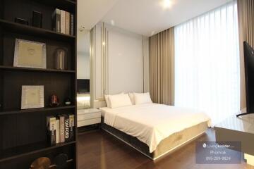 Modern bedroom with a white bed, floor-to-ceiling curtains, a bedside table, and a bookshelf