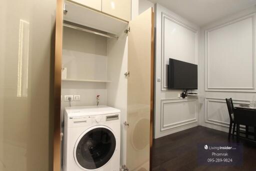 Living area with a washing machine, a wall-mounted TV, and partial view of a dining table