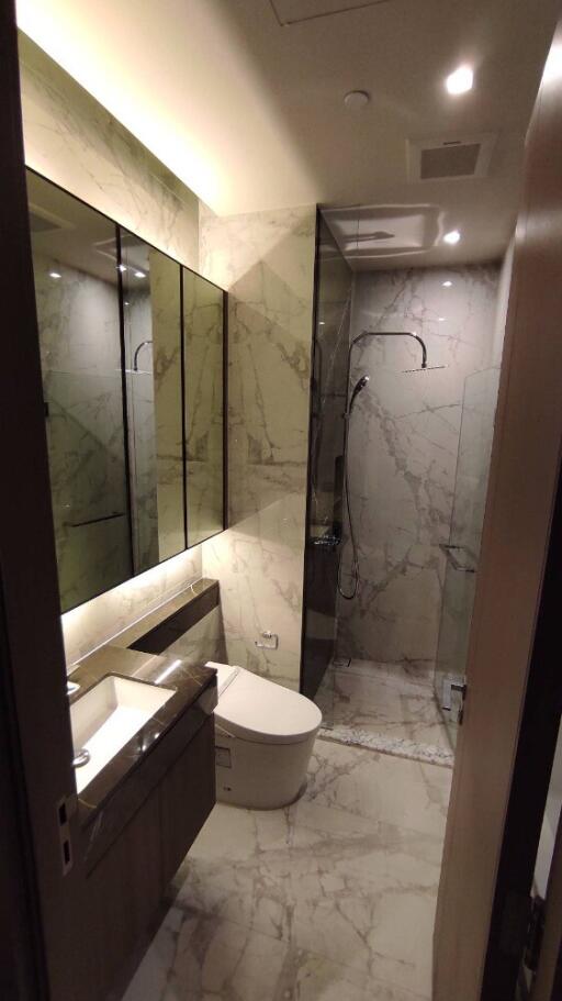 Modern bathroom with marble tiles, glass shower enclosure, and large mirror