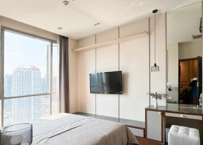 Modern bedroom with a view of the city, featuring a wall-mounted TV and built-in desk.