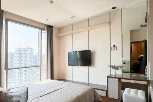 Modern bedroom with a view of the city, featuring a wall-mounted TV and built-in desk.