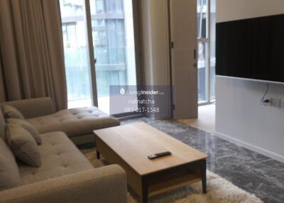 Living room with a sofa, coffee table, wall-mounted TV, and large windows