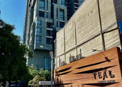 Exterior view of a tall modern residential building with a wooden fence labeled TEAL