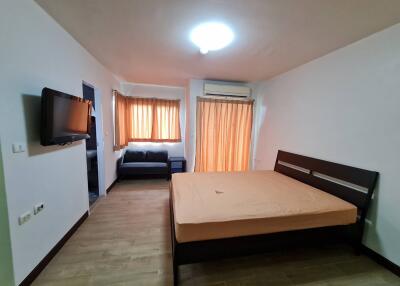 Bedroom with large bed, TV, couch, and windows with curtains