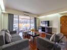 Modern living room with a view, featuring comfortable sofas, a large flat-screen TV, and a wooden coffee table.