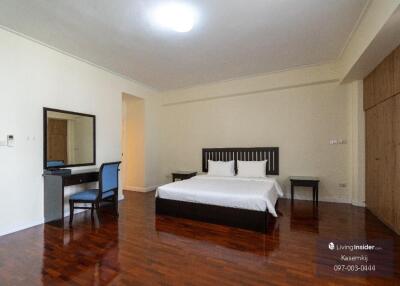 Spacious bedroom with wooden flooring, a bed with white linens, a desk, and built-in wooden wardrobes