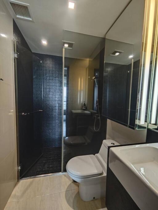 Modern bathroom with black tiled shower, toilet, and sink with vanity mirror