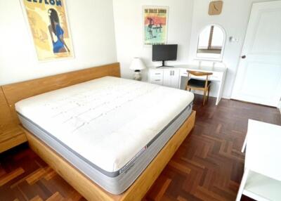 Spacious bedroom with wooden floor, bed, desk, and wall art.