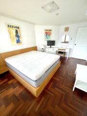 Spacious bedroom with wooden floor, bed, desk, and wall art.