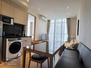 Modern living area with kitchen and dining table, washer and dryer, sofa, TV, and large window