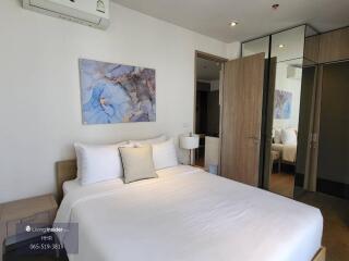 A cozy bedroom featuring a double bed with a white duvet, bedside tables with lamps, a wall-mounted air conditioner, a large mirror, and abstract artwork above the bed.