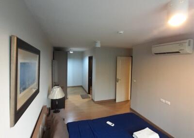 Bedroom with bed, blue bedsheet, wall-mounted air conditioner, and hallway view