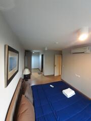 Bedroom with bed, blue bedsheet, wall-mounted air conditioner, and hallway view