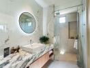 Modern bathroom with marble counter, circular mirror, and glass shower