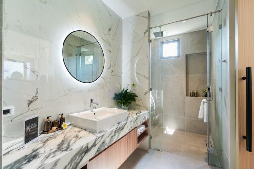 Modern bathroom with marble counter, circular mirror, and glass shower