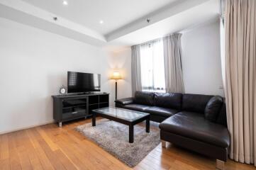 Modern living room with black leather sectional sofa, flat-screen TV, and a floor lamp