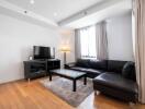 Modern living room with black leather sectional sofa, flat-screen TV, and a floor lamp