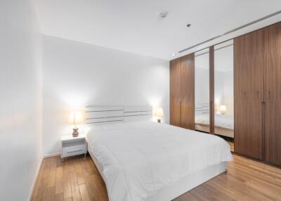 Modern bedroom with wooden flooring, white walls, and large wardrobe