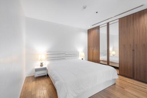 Modern bedroom with wooden flooring, white walls, and large wardrobe