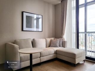 Modern living room with beige sectional sofa, tall glass windows, and city view