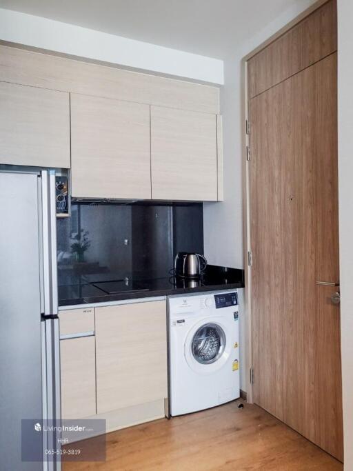 Compact kitchen with wooden cabinetry, stainless steel refrigerator, washing machine, and wood-paneled door