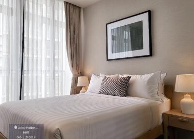 Modern bedroom with a neatly made bed, framed artwork, and bedside lamps