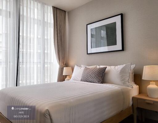 Modern bedroom with a neatly made bed, framed artwork, and bedside lamps