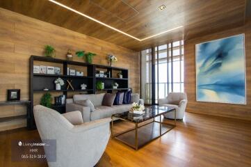 Modern living room with wooden floor, large windows, a bookshelf, and comfortable seating