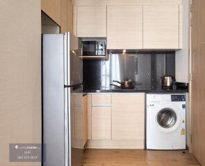 Modern kitchen with light wood cabinets, stainless steel appliances, and washing machine