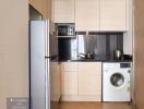 Modern kitchen with light wood cabinets, stainless steel appliances, and washing machine