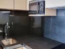 Modern kitchen with black countertop, sink, microwave, and stovetop