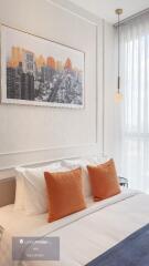 A modern bedroom with cityscape artwork above the bed and orange pillows