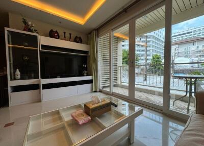 Modern living room with a large TV, decorative shelving, and floor-to-ceiling windows