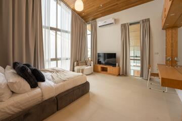 Spacious bedroom with large windows, wooden ceiling, bed, TV, and desk.