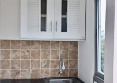 Small kitchenette with upper and lower cabinets, tile backsplash, and a window.