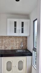 Small kitchenette with upper and lower cabinets, tile backsplash, and a window.