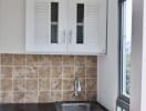 Small kitchenette with upper and lower cabinets, tile backsplash, and a window.