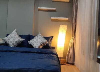 Cozy bedroom with blue bedding, decorative pillows, and a standing lamp