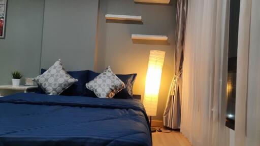 Cozy bedroom with blue bedding, decorative pillows, and a standing lamp