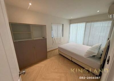 A modern bedroom with a large bed, built-in shelving unit, and natural lighting from wide windows.