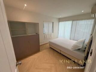 A modern bedroom with a large bed, built-in shelving unit, and natural lighting from wide windows.